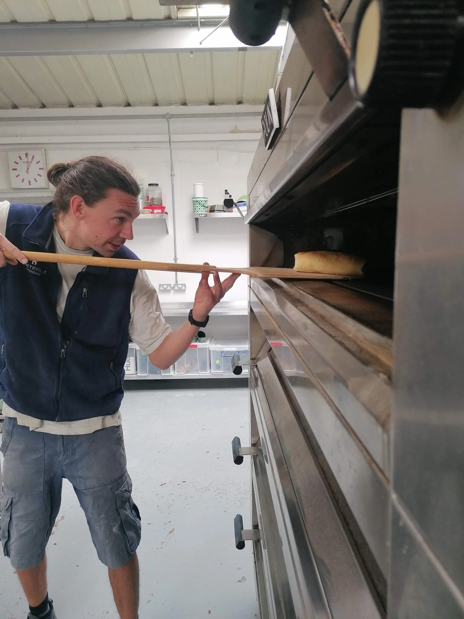 A baker sliding bread into the deck oven with a long peel