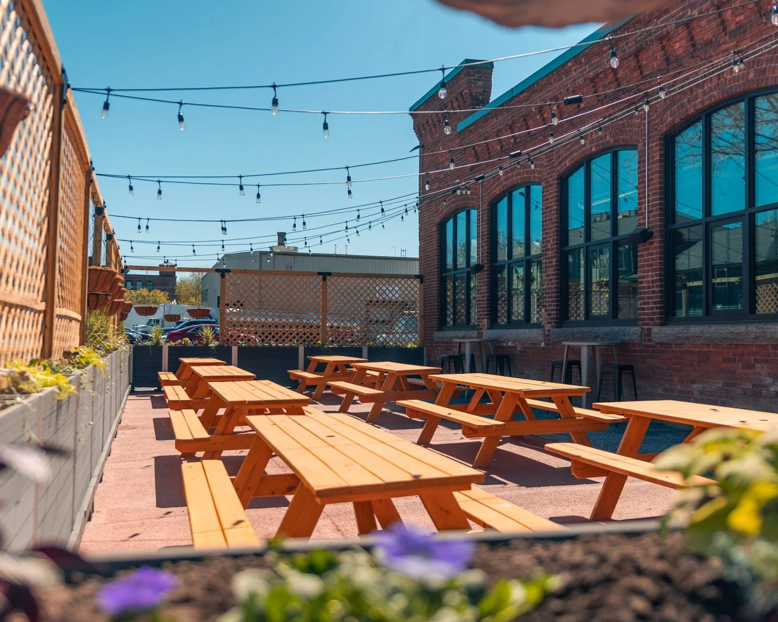 Outdoor picnic tables and string lights beside Burlington Beer Co.’s brick building
