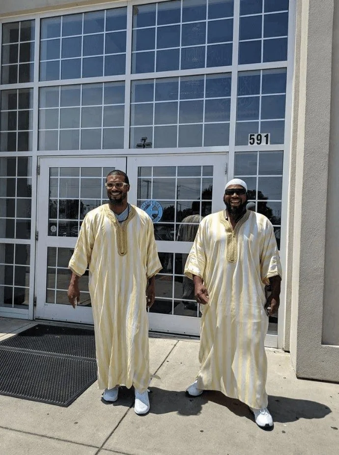 two men in muslim clothing walking out of a building with glass doors smiling