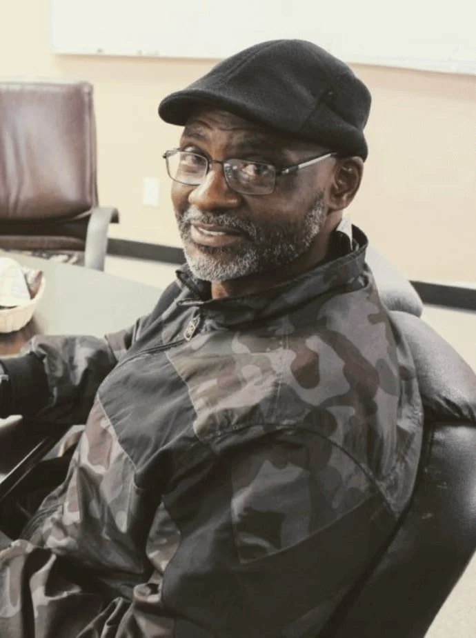 man with black cap and glasses smiles at the camera