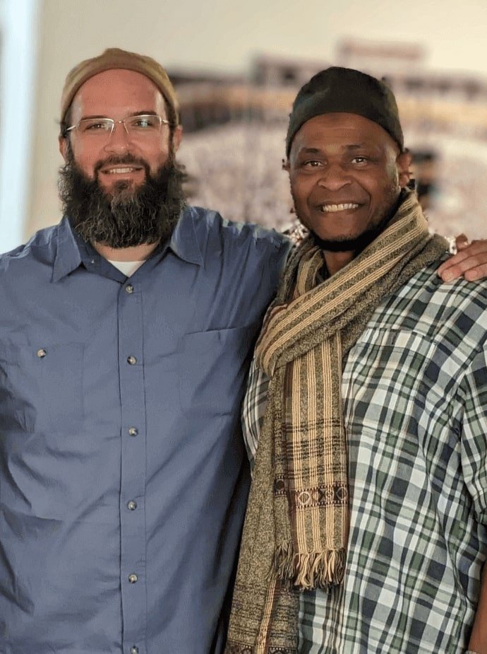 a man with a beard with his arm around man with a striped scarf