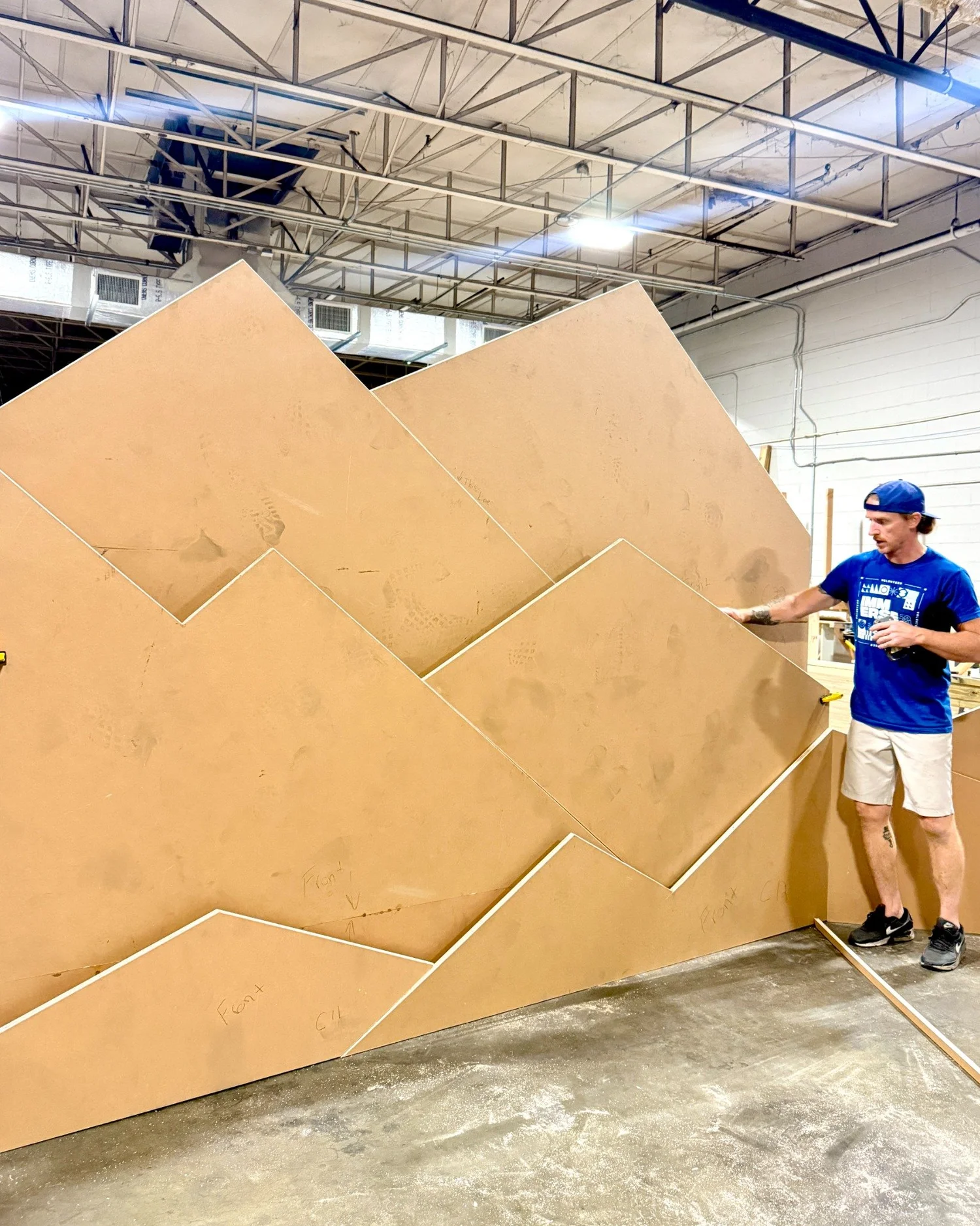 A fabricator standing beside full-scale angular mountain panels in the workshop