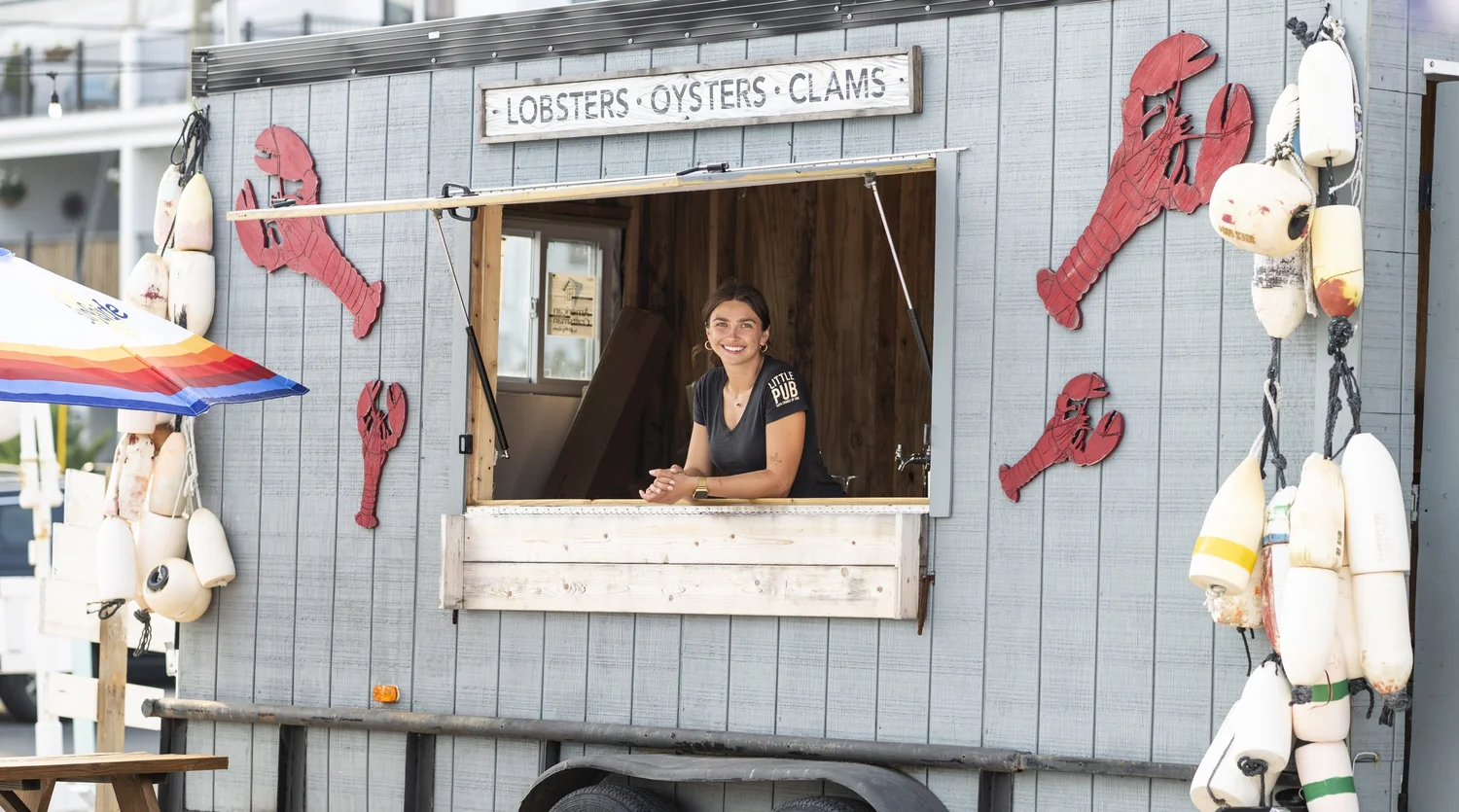 Little Pub staff member at a seafood serving window decorated with lobsters and buoys.