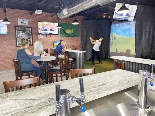 Golfer mid-swing in a simulator bay beside the bar