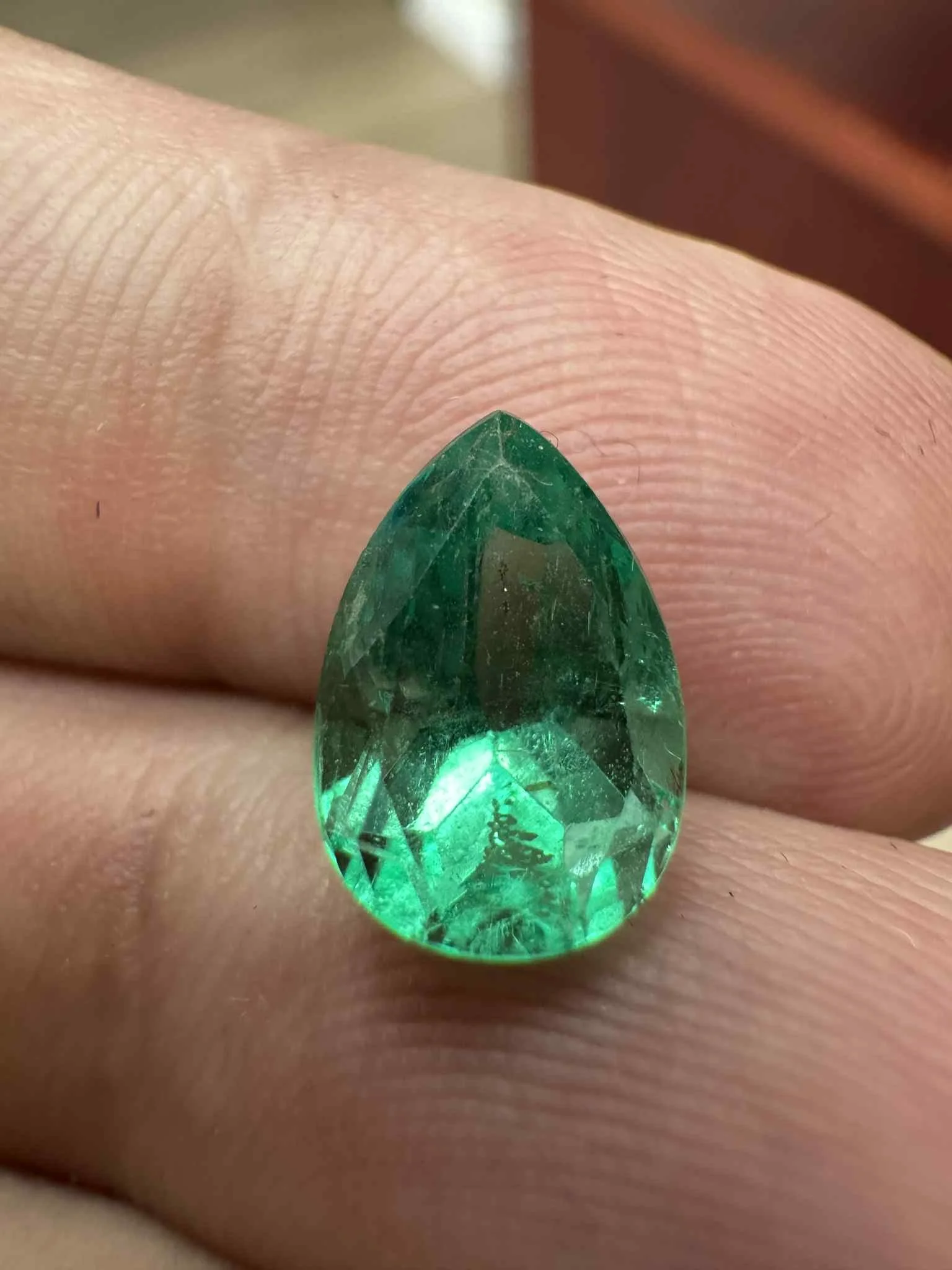 Colombian emerald gemstone held in hand showing deep green glow and natural jardine, sourced by A. D'Mae Diamonds Los Angeles