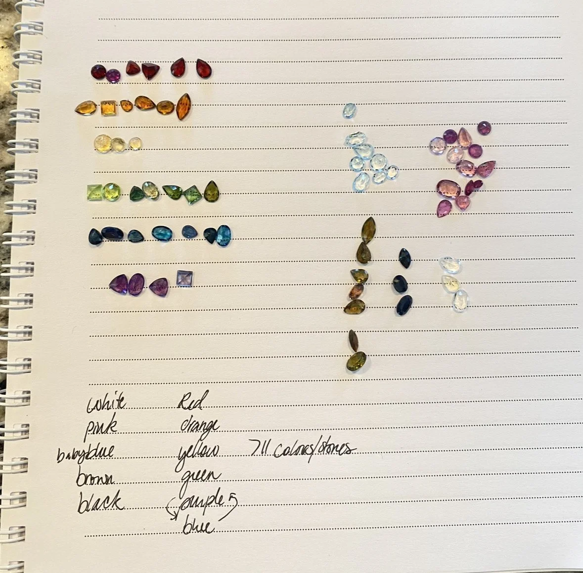 Grandmother's gemstone collection sorted by color on notebook page for custom rainbow pride ring, 11 colors identified, designed by A. D'Mae Diamonds Los Angeles