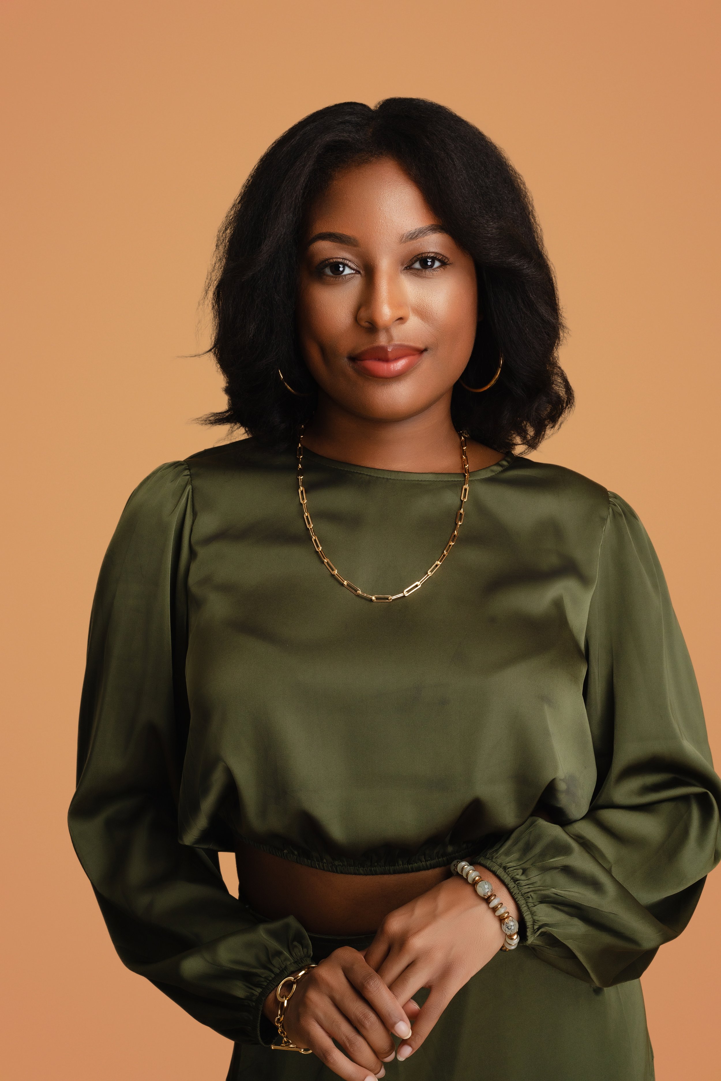 Headshot of a woman with a soft smile, gold jewelry, and a peach background.