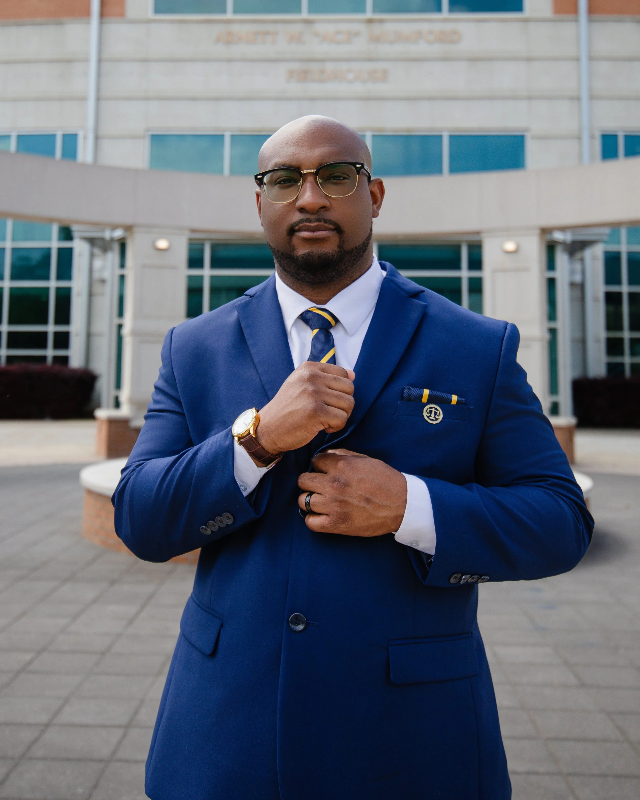 Headshot of a male in a deep blue suit holding his lapel.