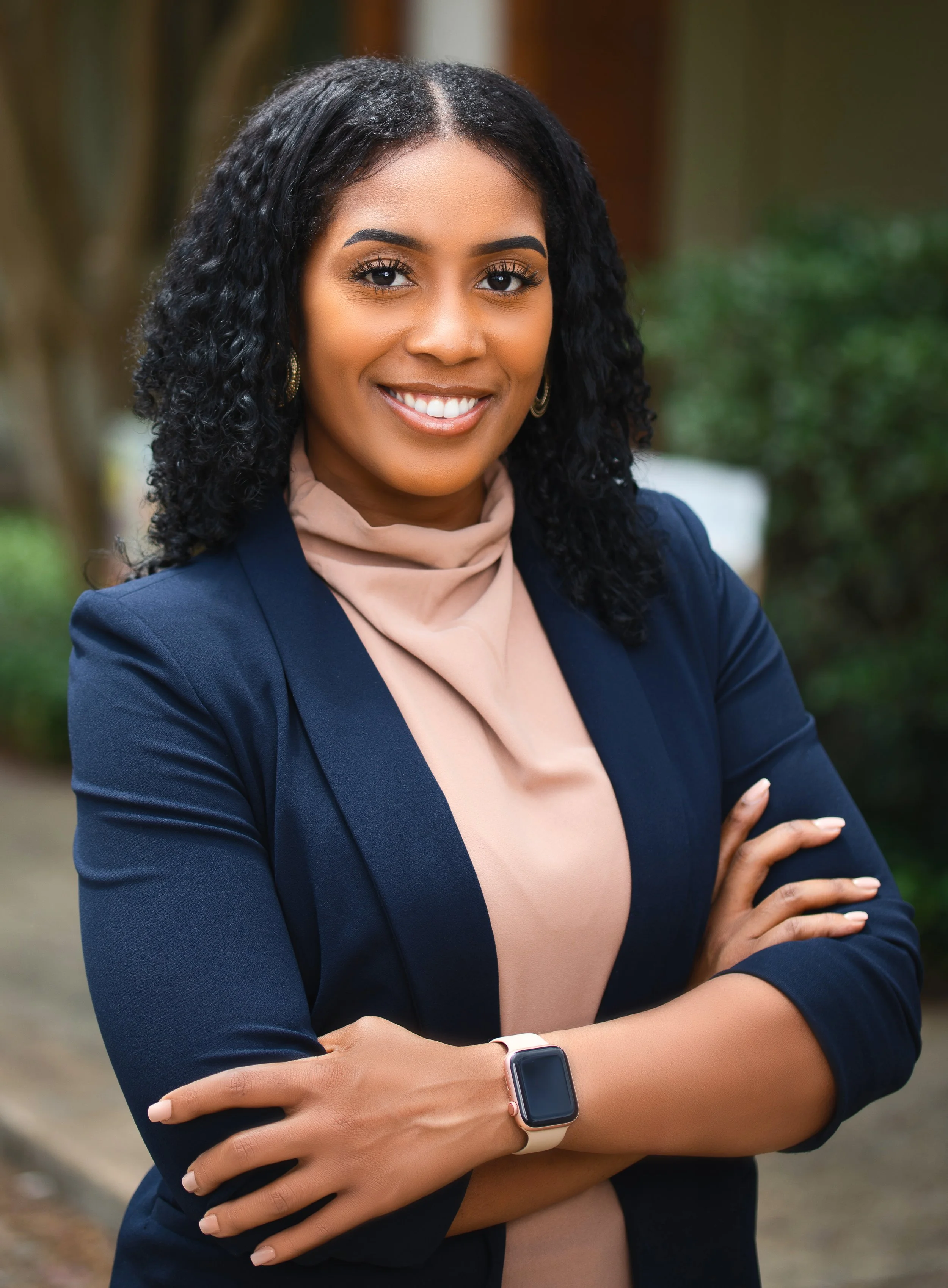 Headshot of an educator with wavy hair, a pick top, and a navy blue blazer.