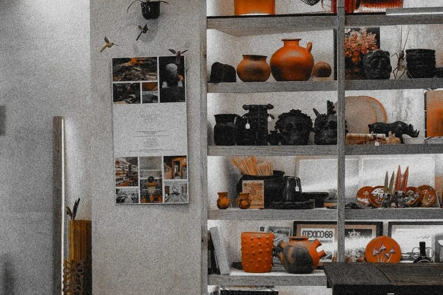 Interior de Proyectos Paraíso: anaquel con piezas de barro negro y naranja, fotografías en la pared.