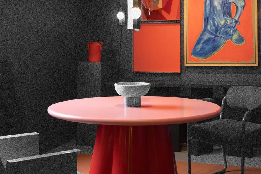 Interior de Originario: mesa redonda roja, silla negra y dos cuadros de colores sobre muro oscuro.