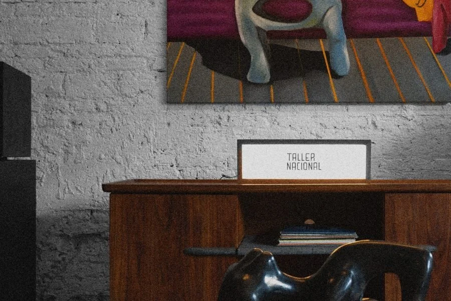 Interior de Taller Nacional: escritorio de madera con una escultura negra, un cuadro y un letrero con el nombre del taller.