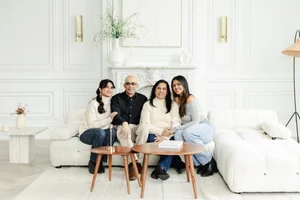Parents and their two adult daughters sit together on a white sofa in a bright, panelled studio living room.