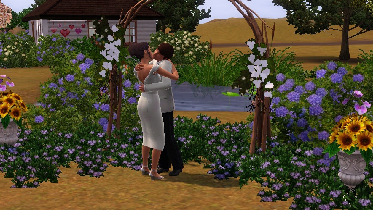 Dorothy and Matthew embracing and kissing in front of an arch made of branches, surrounded by flowers