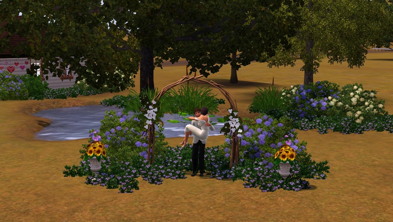 Matthew holds Dorothy in his arms with one arm behind her knees and the other supporting her back. She has her arms around his shoulders, and they’re under a wedding arch made of branches, surrounded in flowers, in front of the pond in the Tevellyn family's backyard.