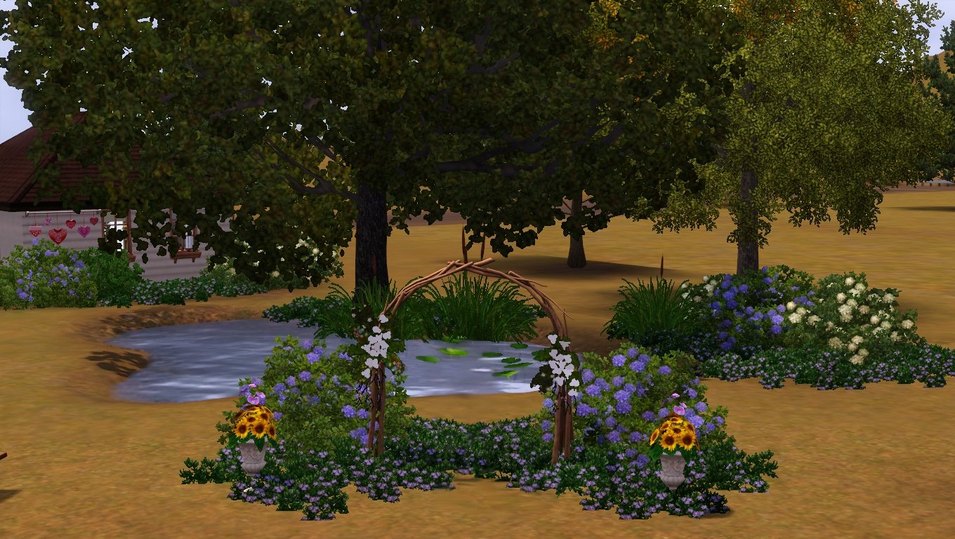 An arch made of branches, decorated with and surrounded by flowers at the edge of a pond