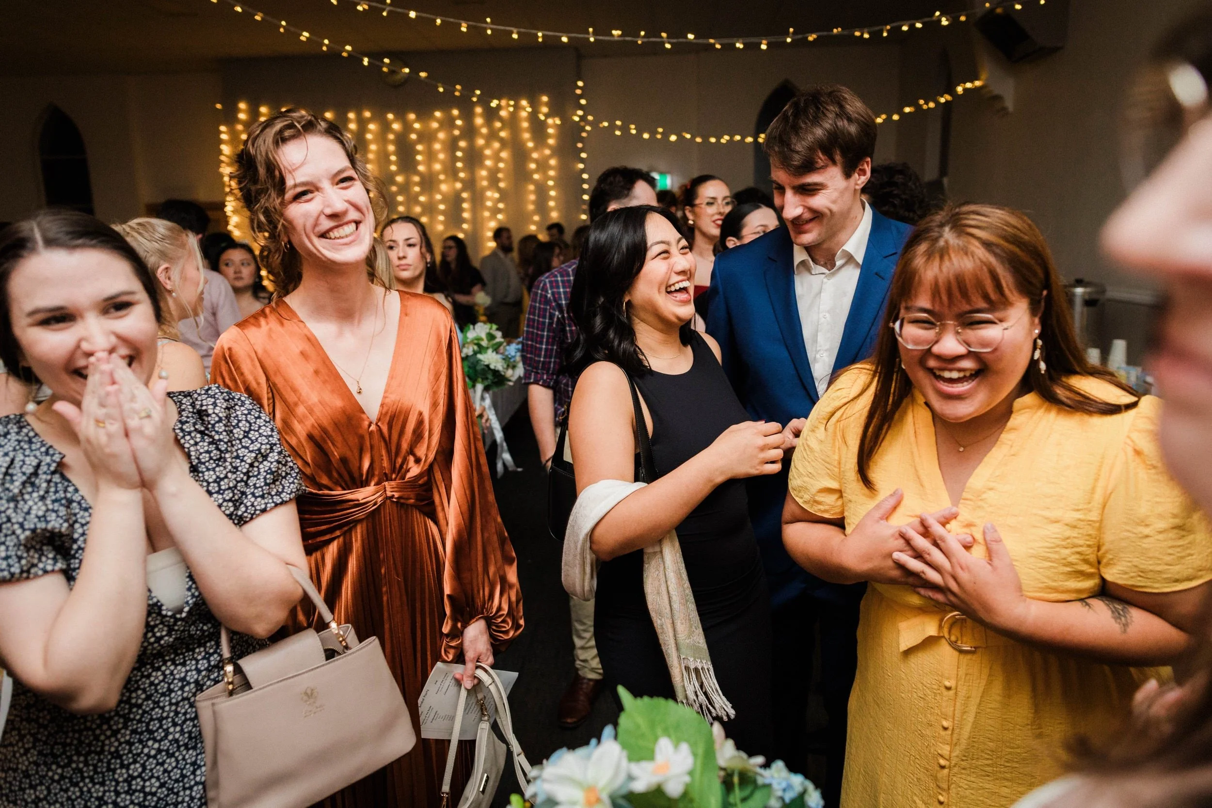 Long dinner table full of guests laughing under warm light