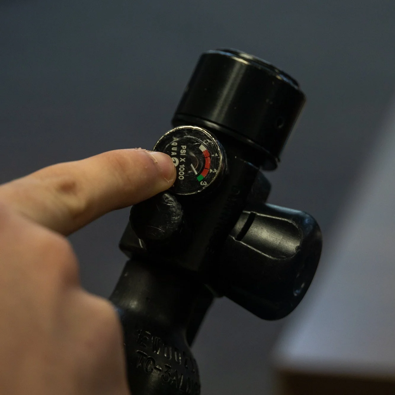 Close-up of a hand checking the pressure gauge on an emergency breathing cylinder
