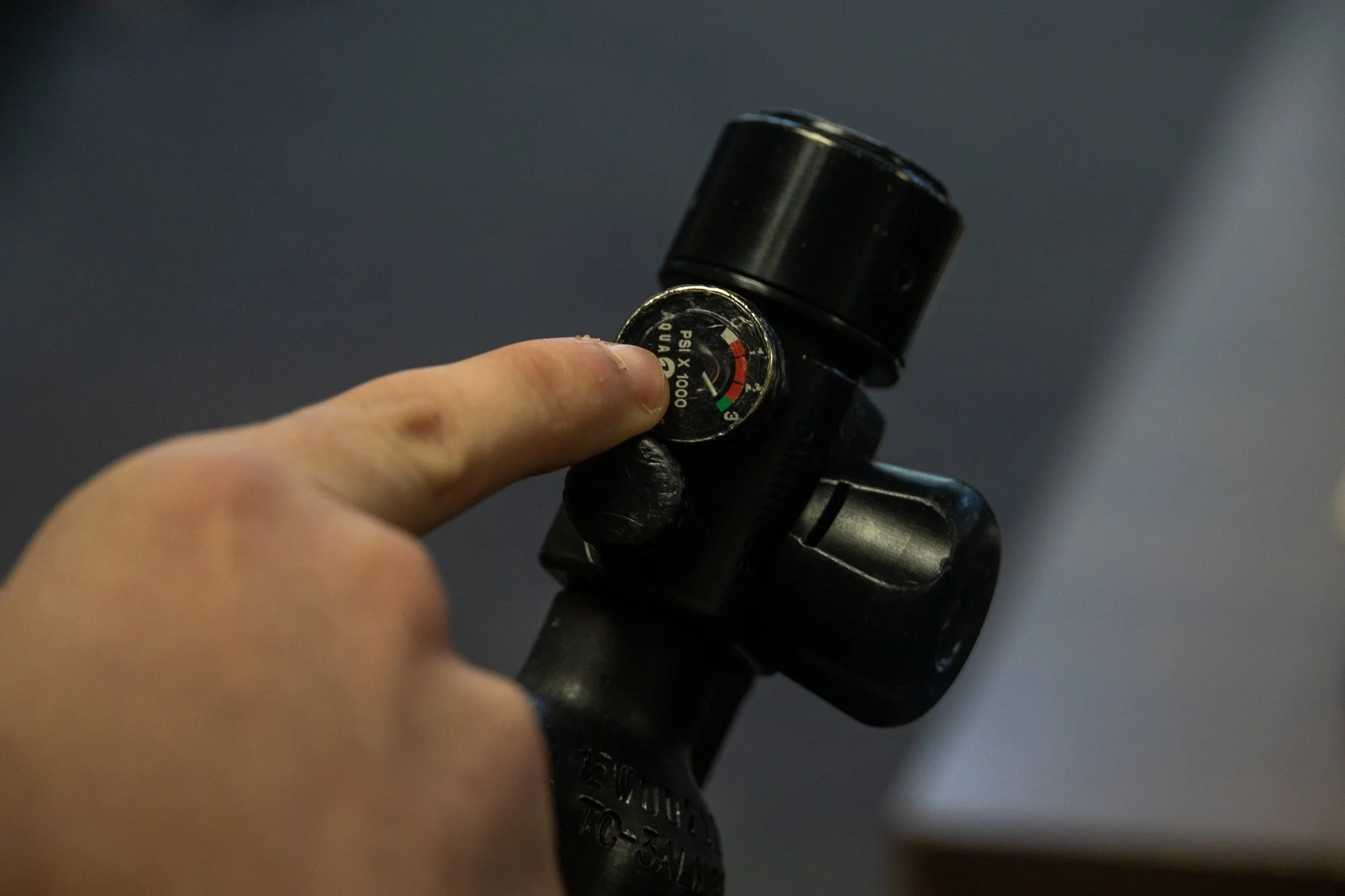 A hand checks the pressure gauge on an emergency breathing cylinder during underwater egress training