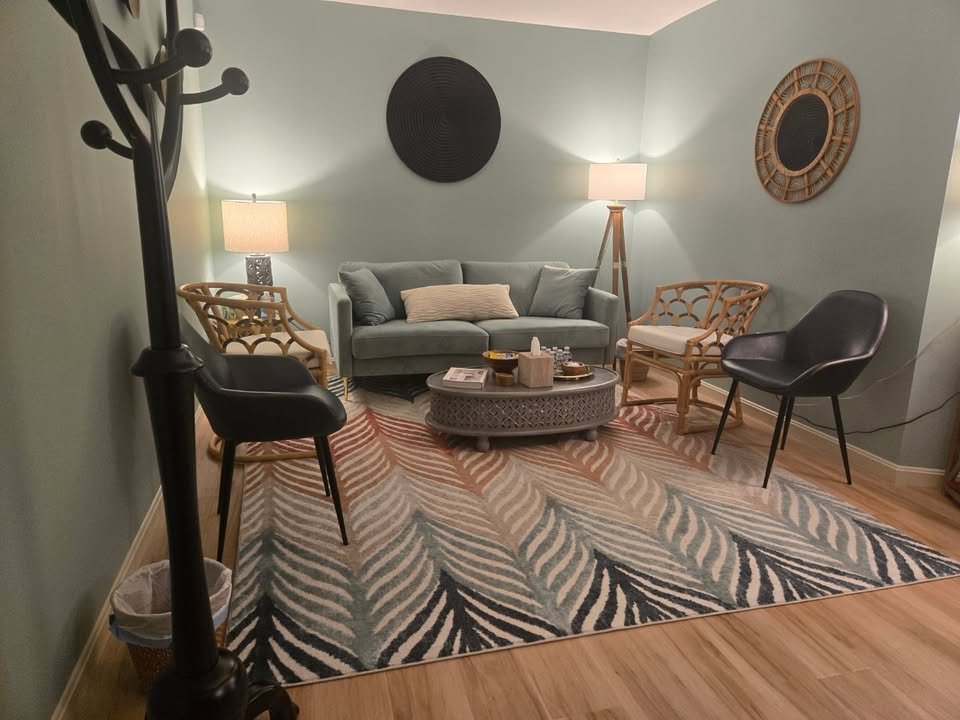 The waiting area at Meadow Grove Counseling, featuring a teal sofa, rattan chairs, warm lighting, and a patterned rug on hardwood floors