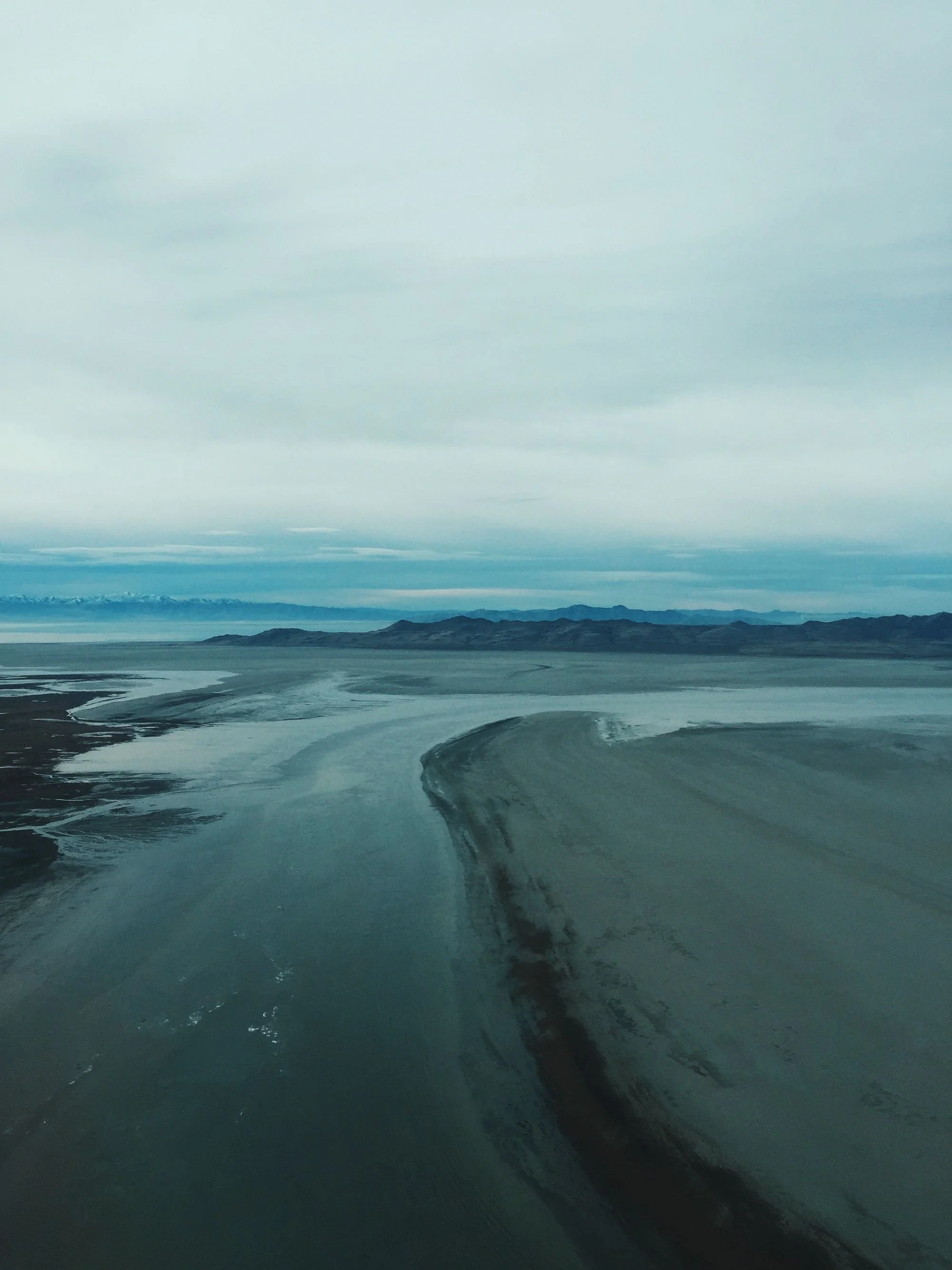 Aerial view of salt flats and mountains under an overcast sky