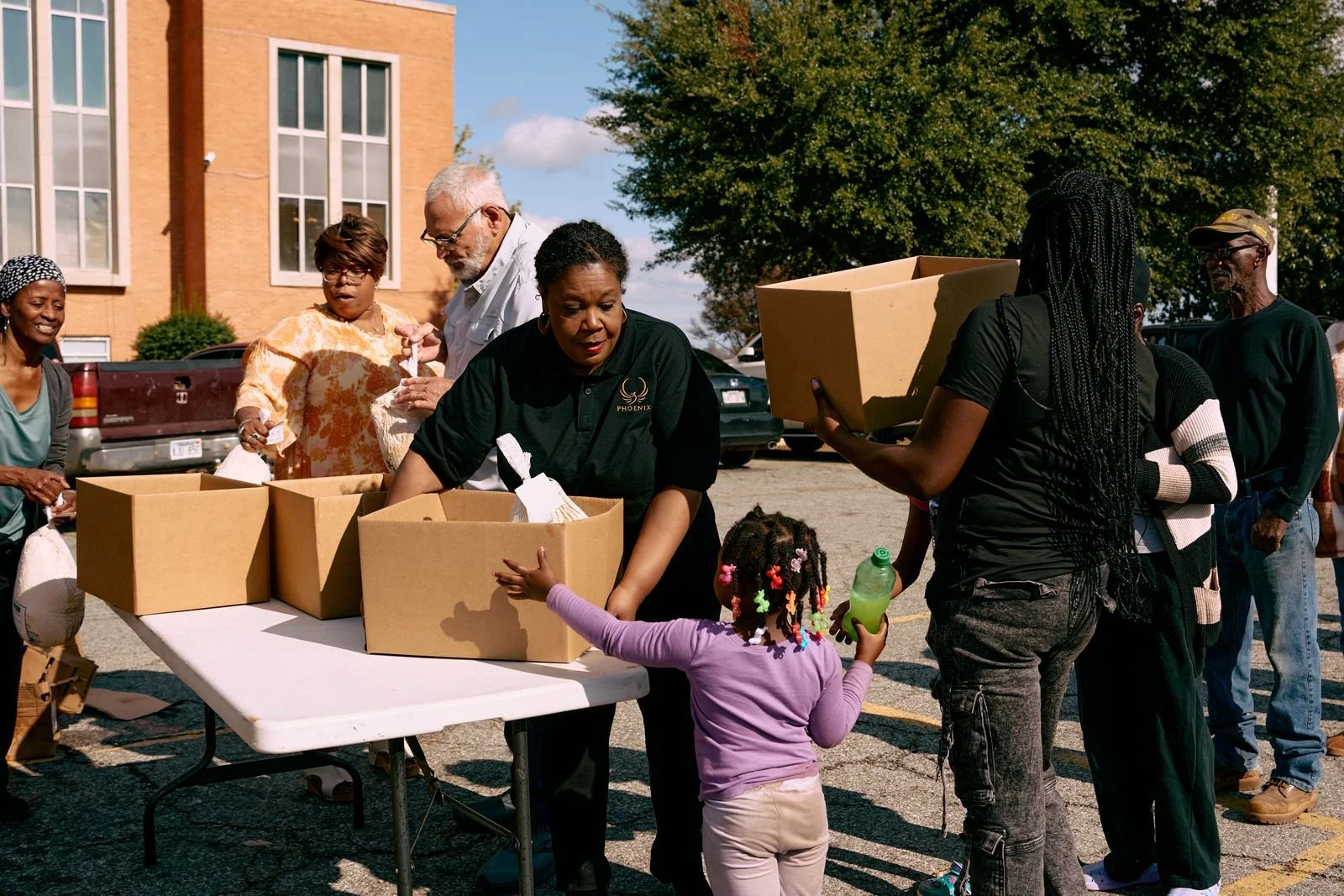 A Phoenix staff member hands a Gratitude Week meal box to a young girl as neighbors wait in line