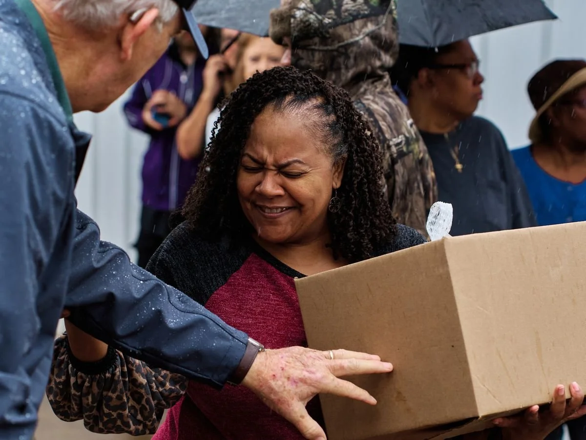 A neighbor laughs as she receives her Gratitude Week meal box in the rain