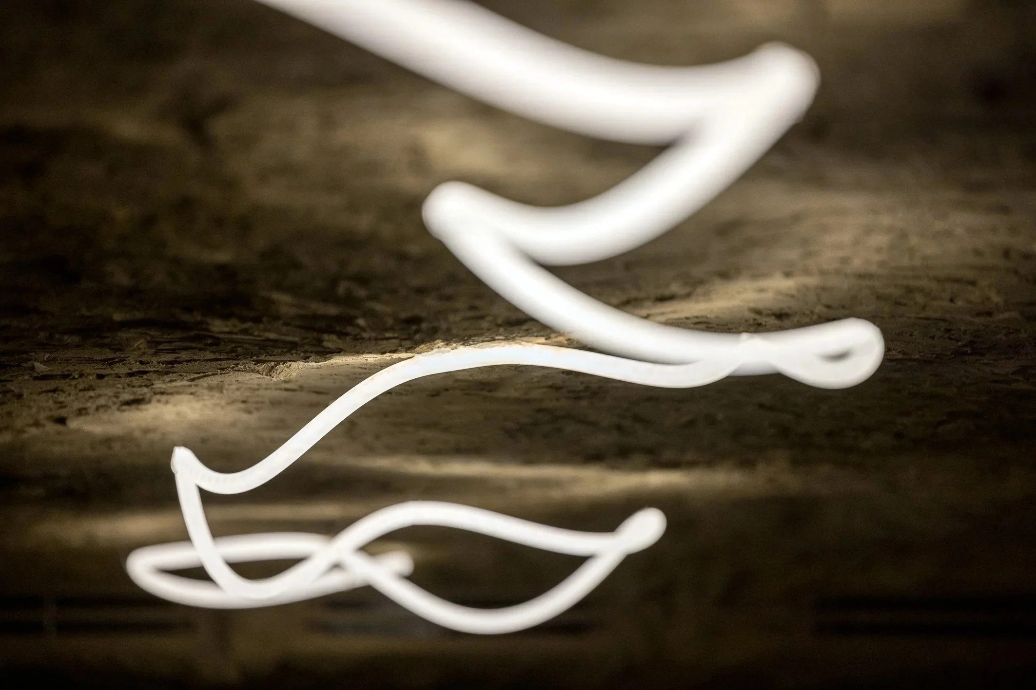 Abstract close-up of a sculptural wavy LED ceiling light set against a textured stone ceiling, creating a modern architectural lighting feature.