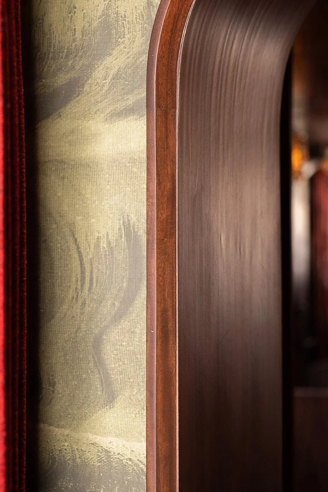 Close-up of a curved dark wood booth partition beside a red velvet curtain, highlighting the restaurant's warm materials and textured wall finish.