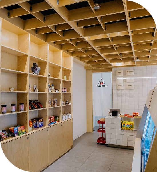 The interior of Onigiri Co., with wooden cubbies and shelves lining the back wall, a similar wooden grid pattern extending to the ceiling, large grey floor tiles, and a white square tile counter in front of a white square tiled wall.