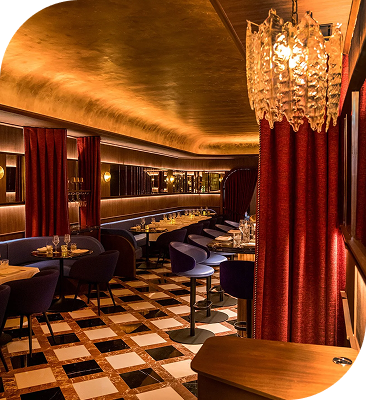 Elegant restaurant dining room with red curtains, purple seating, patterned floors and warm ambient lighting.