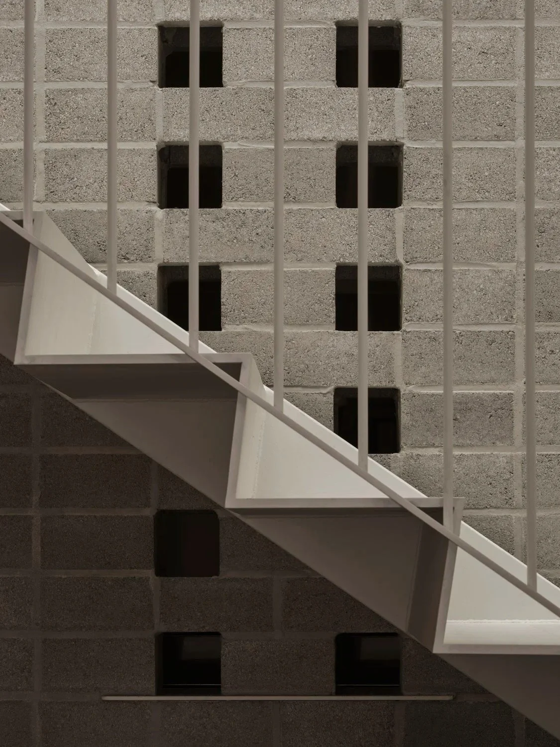 Architectural detail of a white steel staircase set against a decorative concrete block wall with geometric openings in a minimalist restaurant interior.