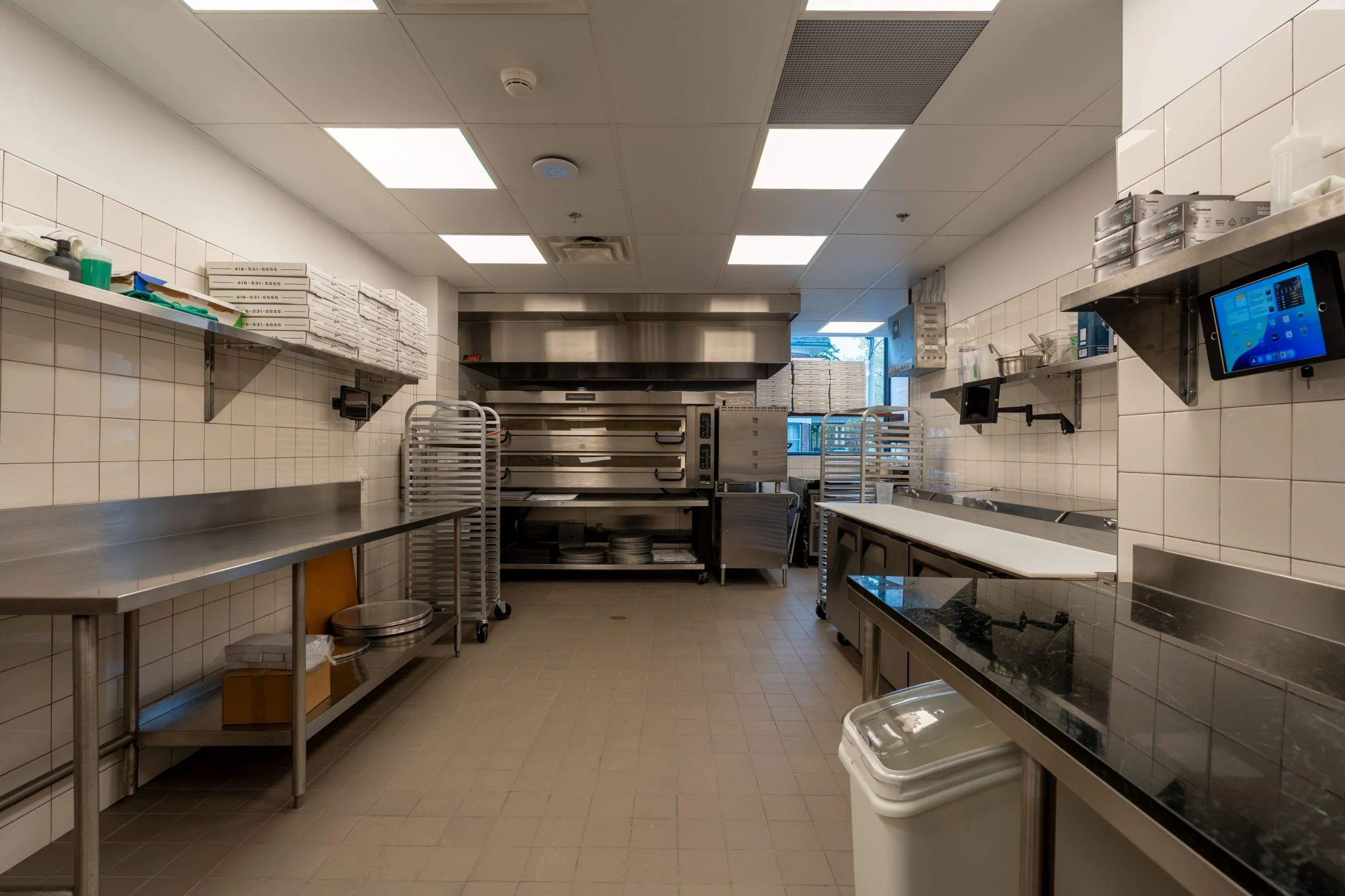 Commercial kitchen at Pizzeria Badiali with stainless steel prep tables, pizza ovens and storage racks.