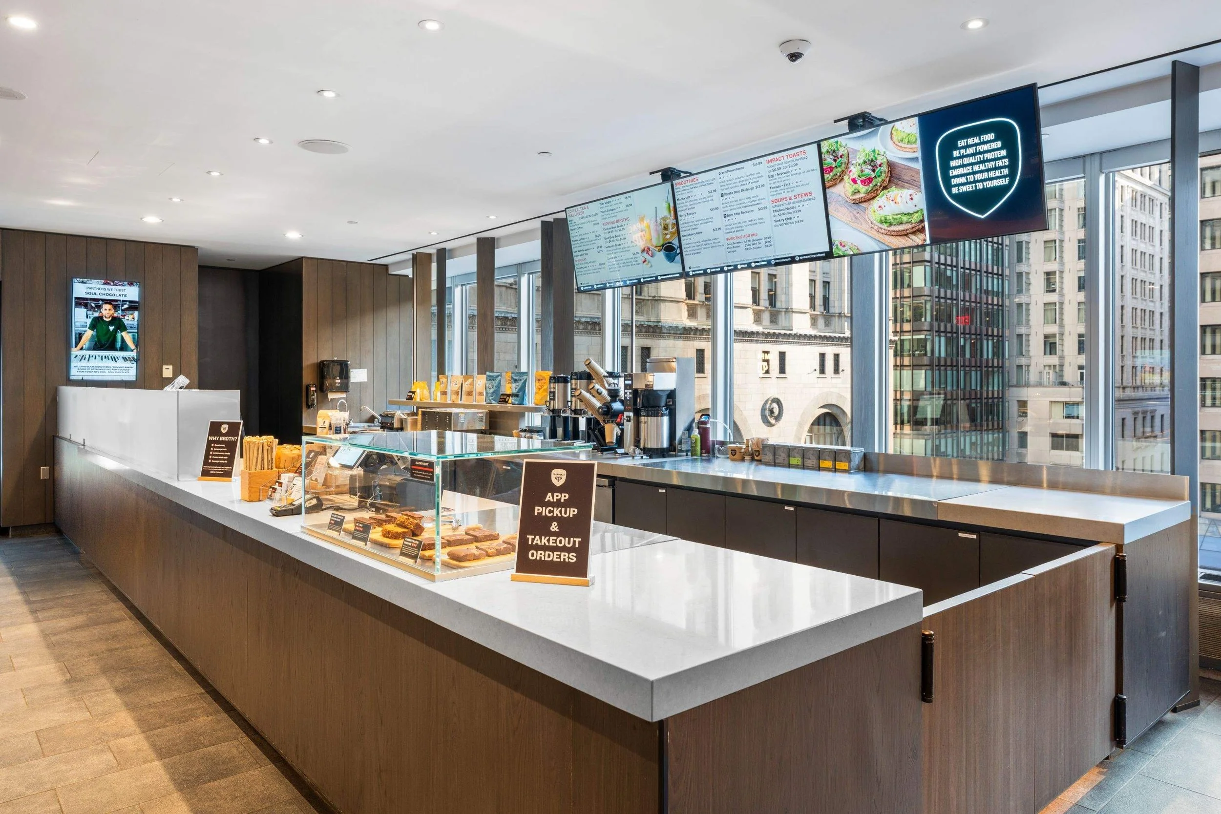 Modern Impact Kitchen service counter with food display case, digital menu boards, coffee equipment, and large windows.