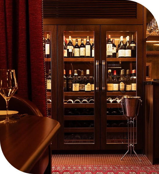 Illuminated wine cabinet in an elegant restaurant interior with rich wood finishes and red accents.