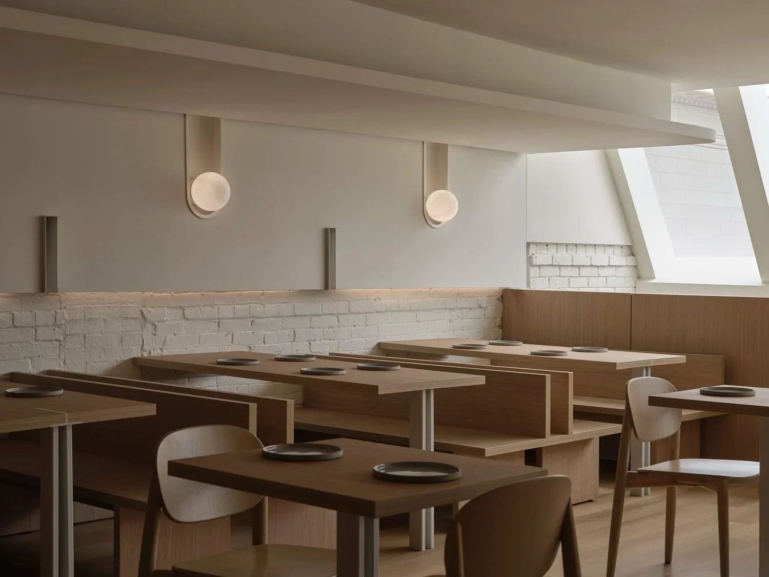 Wide view of minimalist restaurant interior with chef's counter, custom seating, and exposed brick accents.