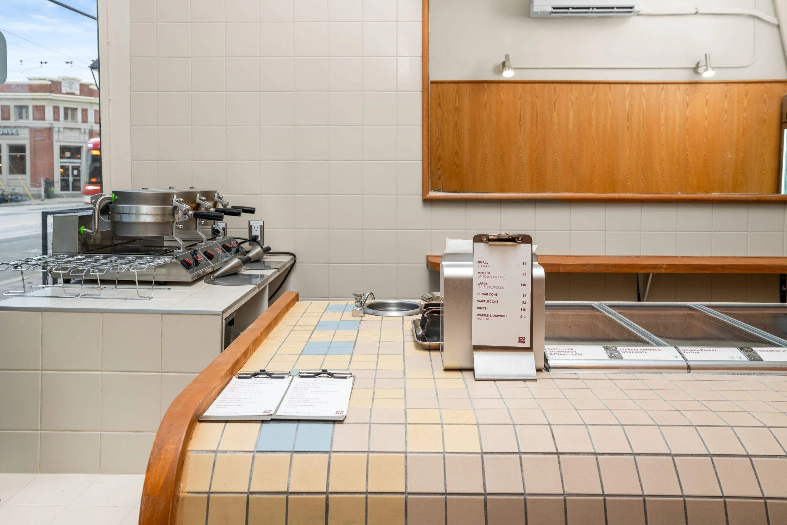 Tiled Cono service counter with menu display, gelato case and waffle-making equipment.