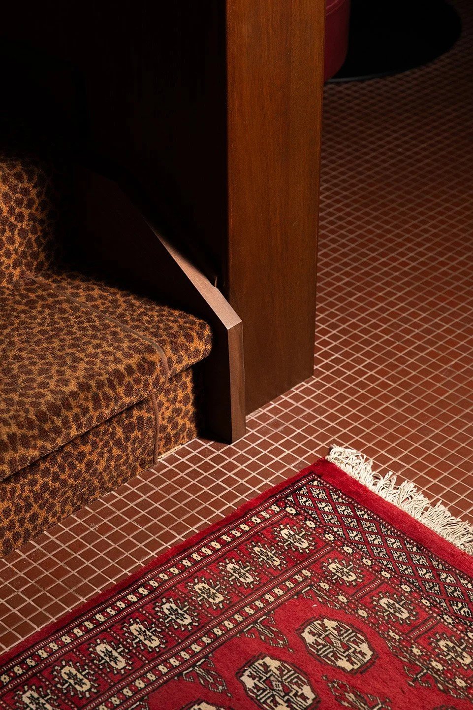 Close-up of a restaurant interior featuring a leopard-print upholstered booth, warm wood paneling, a red patterned area rug, and small square mosaic floor tiles.