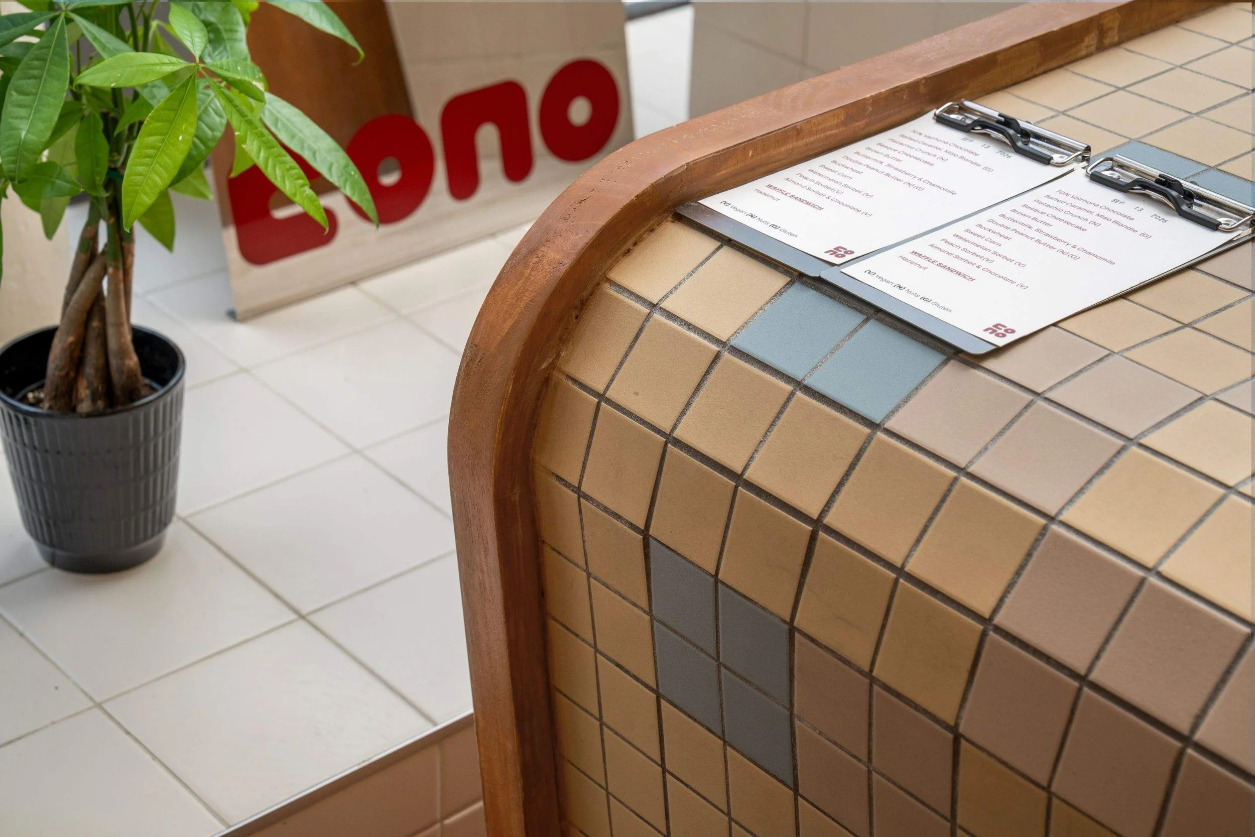 Close-up of Cono’s curved tiled counter with menu cards and wood trim.