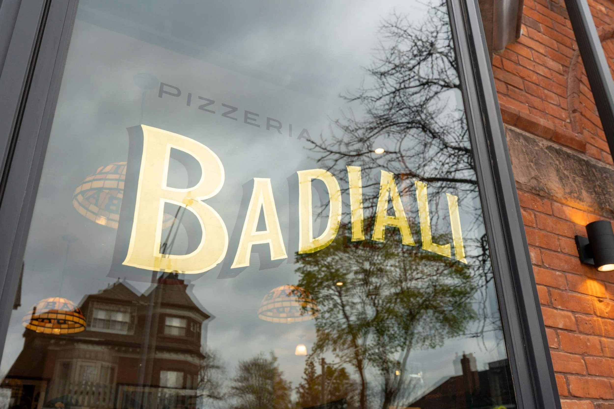 Close-up of the Pizzeria Badiali logo painted on the restaurant’s front window.