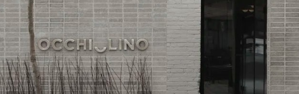 Occhiolino lettering pictured on exterior brick wall beside a black door.