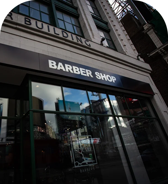 The exterior of Dundas Square Barbers, with tall dark sleek windows and a black faucade on an old grey stone building