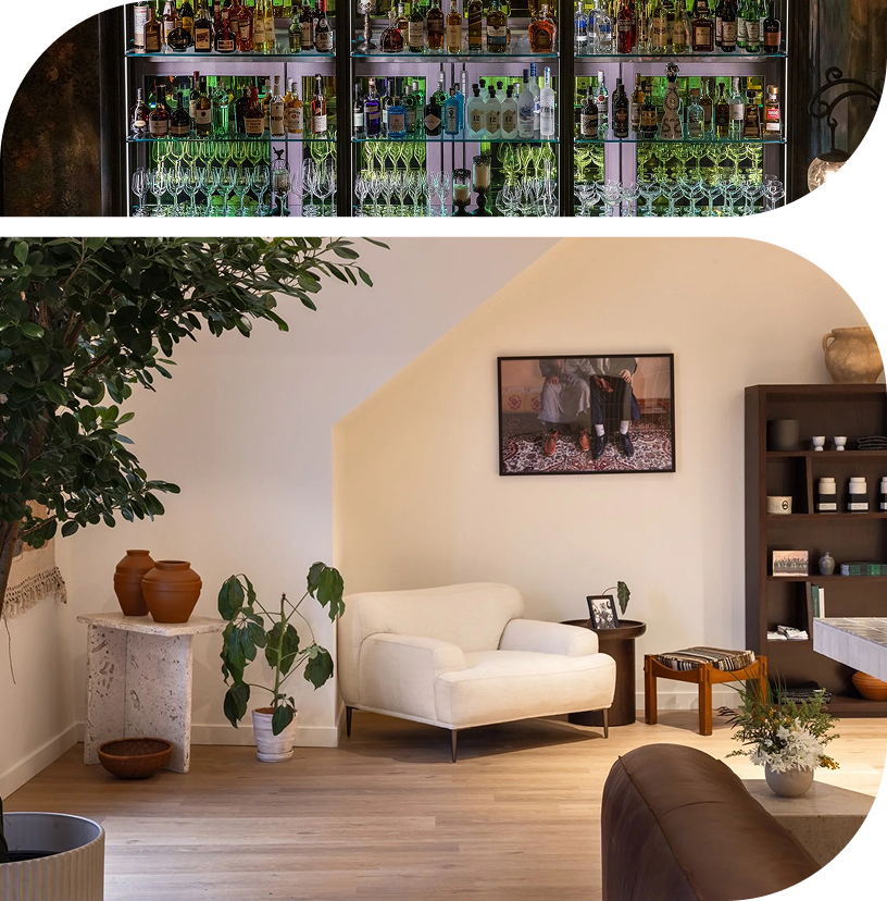 Modern residential interior with a white armchair, natural wood flooring, indoor plants and custom shelving beneath a stocked bar display.