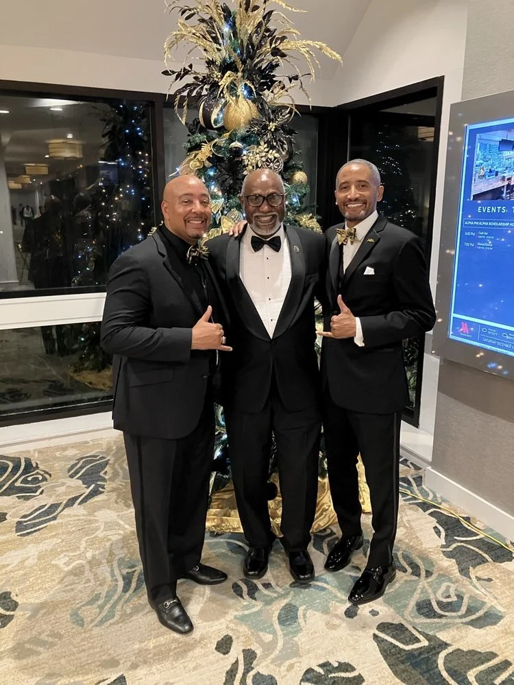 Three brothers in tuxedos in front of the black and gold Christmas tree