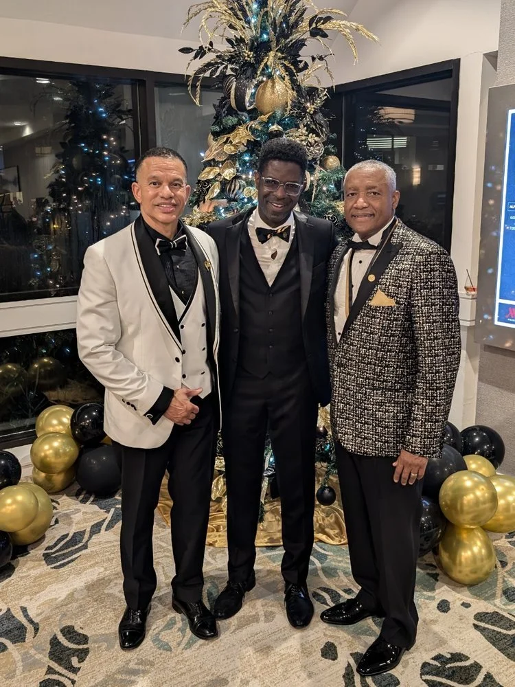 Three brothers in formalwear beside gold and black balloons
