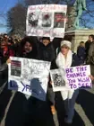 Participants carrying handmade signs at an outdoor advocacy gathering.