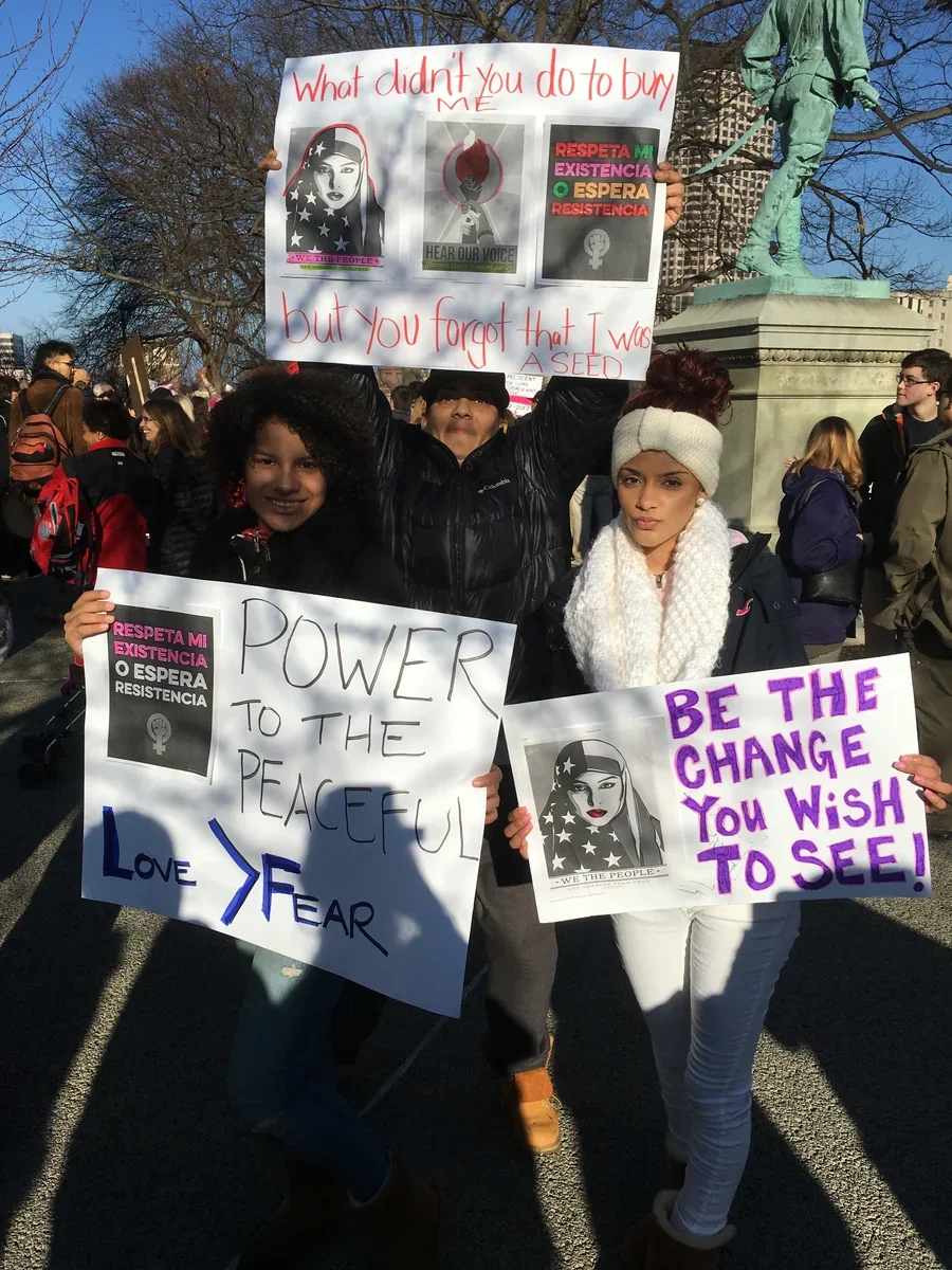 Participants carrying handmade signs at an outdoor advocacy gathering.
