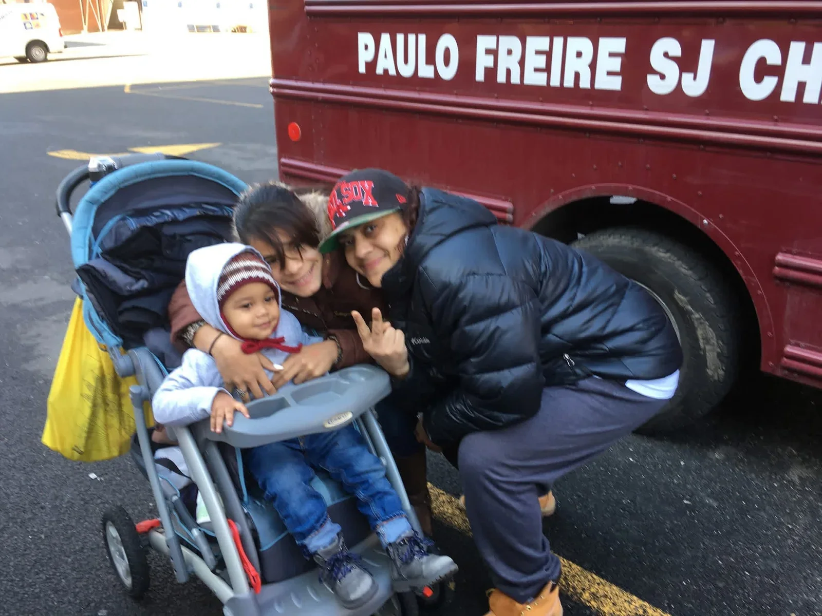 Two adults and a baby beside a red school bus.