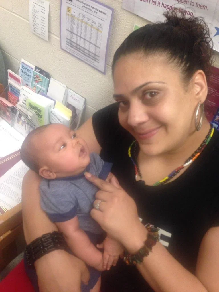 An adult holding a baby beside a window.