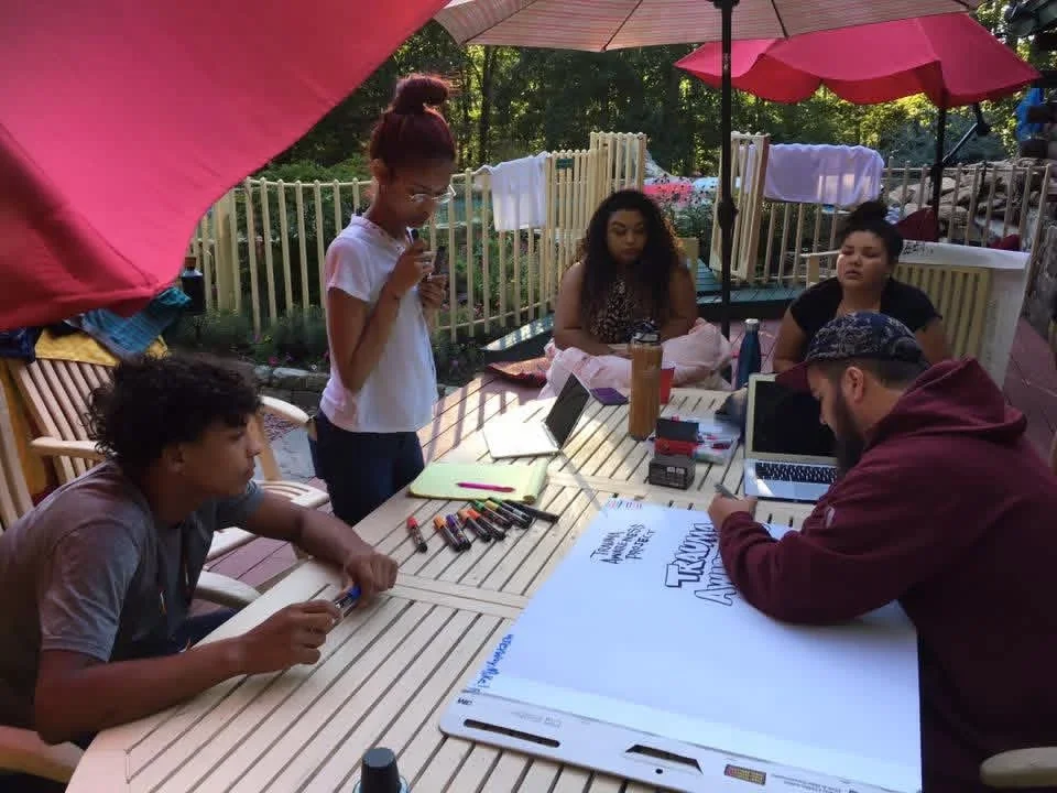 Participants making posters around an outdoor table beneath umbrellas.